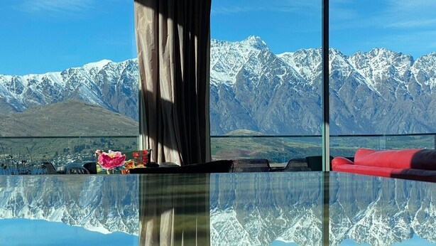 A room with a glass floor reflecting a mountain landscape, a red sofa, and a table with flowers. - 7Manata - Amazing 270deg views! Golf & Ski 10bedrm/8bathrm + 4x seven-seat 4WD's (Fernhill)