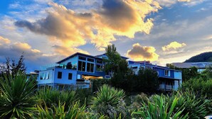 A modern two-story house with large windows and a balcony, surrounded by lush greenery. - 7Manata - Amazing 270deg views! Golf & Ski 10bedrm/8bathrm + 4x seven-seat 4WD's (Fernhill)