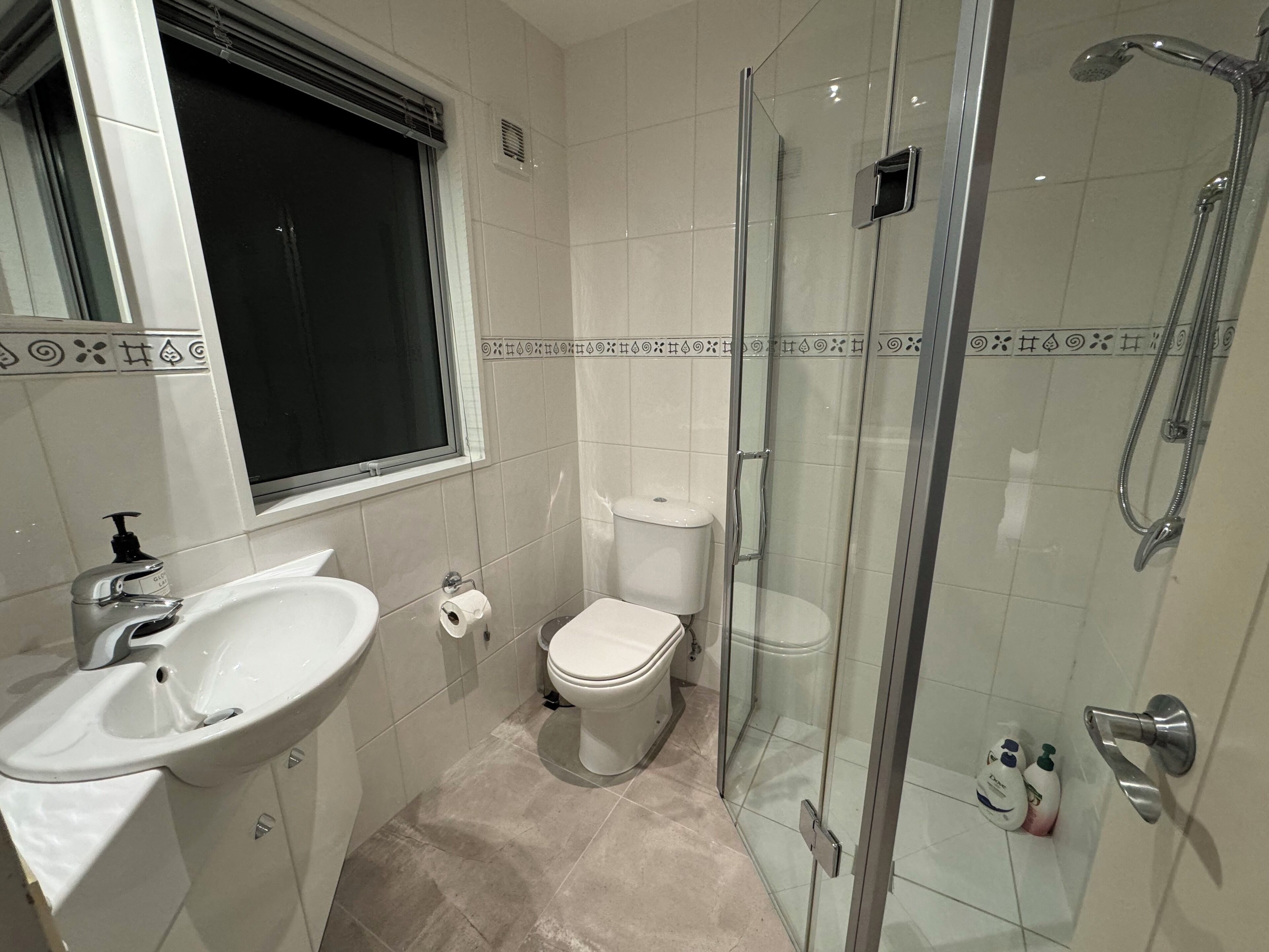 A bathroom with a glass-enclosed shower, a toilet, and a sink.