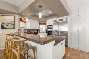 A modern kitchen with a central island, white cabinetry, stainless steel appliances, and a wooden bar stool seating area.