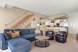 A living room with a blue sectional sofa, two leather armchairs, a coffee table, and a wooden staircase.