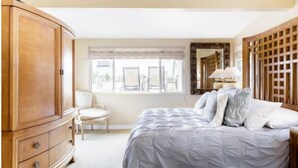 A bedroom with a large bed, a wooden wardrobe, a chair, and a window with a view. - Seaside Home - Full home rental - Beachfront, Full Beach Front Home - 2002 W. Oceanfront (Newport Beach)