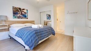 Een slaapkamer met een bed, een plafondventilator, een kunstwerk aan de muur, een nachtkastje met een lamp en een deur.