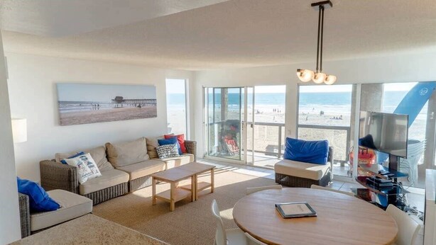 Een moderne woonkamer met een zithoek, een eettafel en een groot raam met uitzicht op het strand.