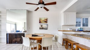 Een moderne keuken met witte kasten, een houten eettafel en een plafondventilator.