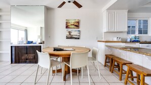 A modern kitchen with white cabinets, a wooden dining table, and a ceiling fan.