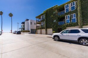 Un bâtiment moderne doté d’une porte de garage, une voiture blanche garée devant, et des palmiers en arrière-plan.