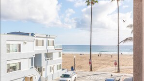 Un edificio de varios pisos con un estacionamiento al frente, una playa con palmeras y el océano al fondo.
