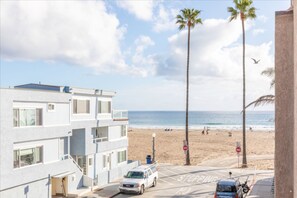 Un edificio de varios pisos con un estacionamiento al frente, una playa con palmeras y el océano al fondo.