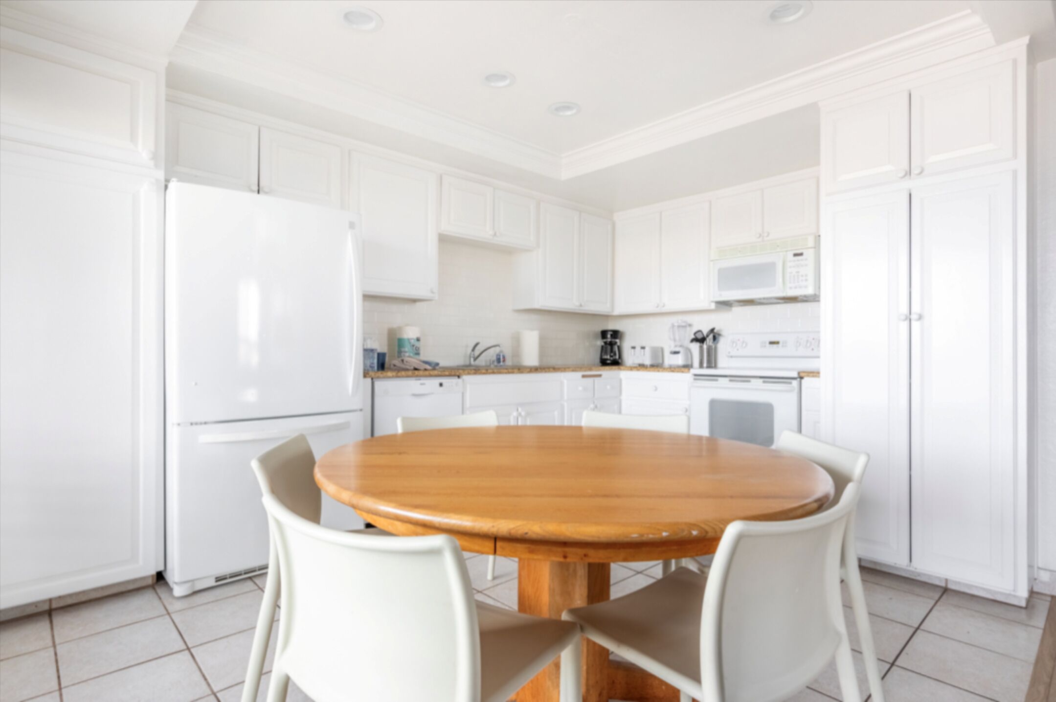 A modern kitchen with white cabinets, a wooden dining table, and white chairs.