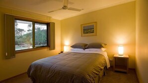 Een slaapkamer met een bed, twee bedlampen, een plafondventilator en een raam met uitzicht op bomen.