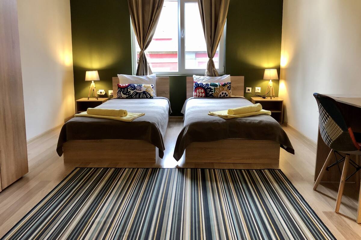 A twin room with two beds, a striped rug, and a desk with a chair.