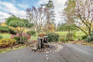 Stroll through a serene garden surrounded by lush trees and a beautifully manicured hedge, with a charming stone structure and paved walkway.