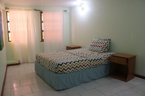 A bedroom with a bed, a nightstand, a window with curtains, and a wall-mounted light. - La Gaviota (Gros Islet)