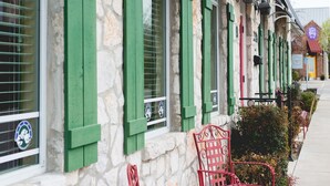 A stone building with green shutters and red metal furniture outside. - High Cotton Inn (New Braunfels)