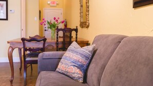 A living room with a gray sofa, a patterned throw pillow, a wooden dining table with chairs, and a vase with flowers. - High Cotton Inn (New Braunfels)