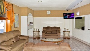 A living room with a brown sofa, a brown armchair, a glass coffee table, and two decorative side tables. - Hotel Baeza (Delicias)
