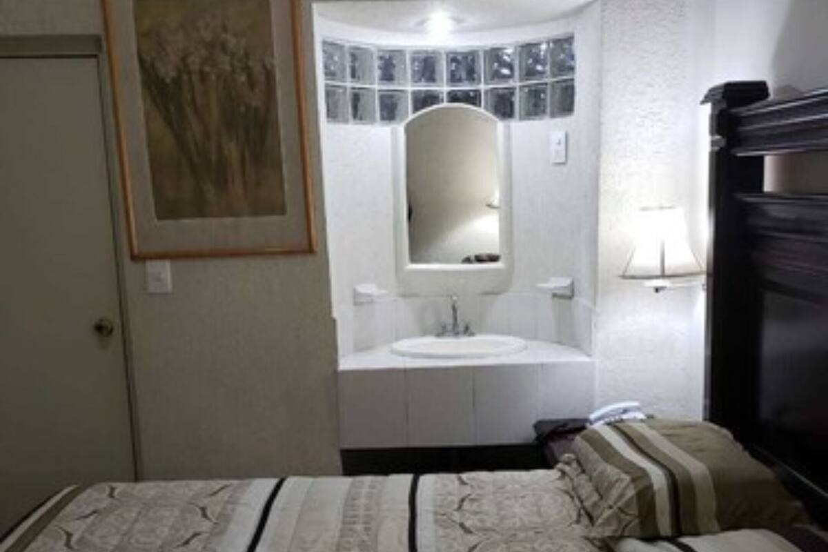 A bedroom with a bed, a bedside table, a mirror, a window, and a wall-mounted air conditioner.
