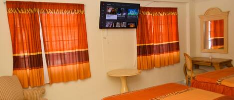 A hotel room with two beds, a television mounted on the wall, a small round table, a chair, and curtains with a striped pattern.