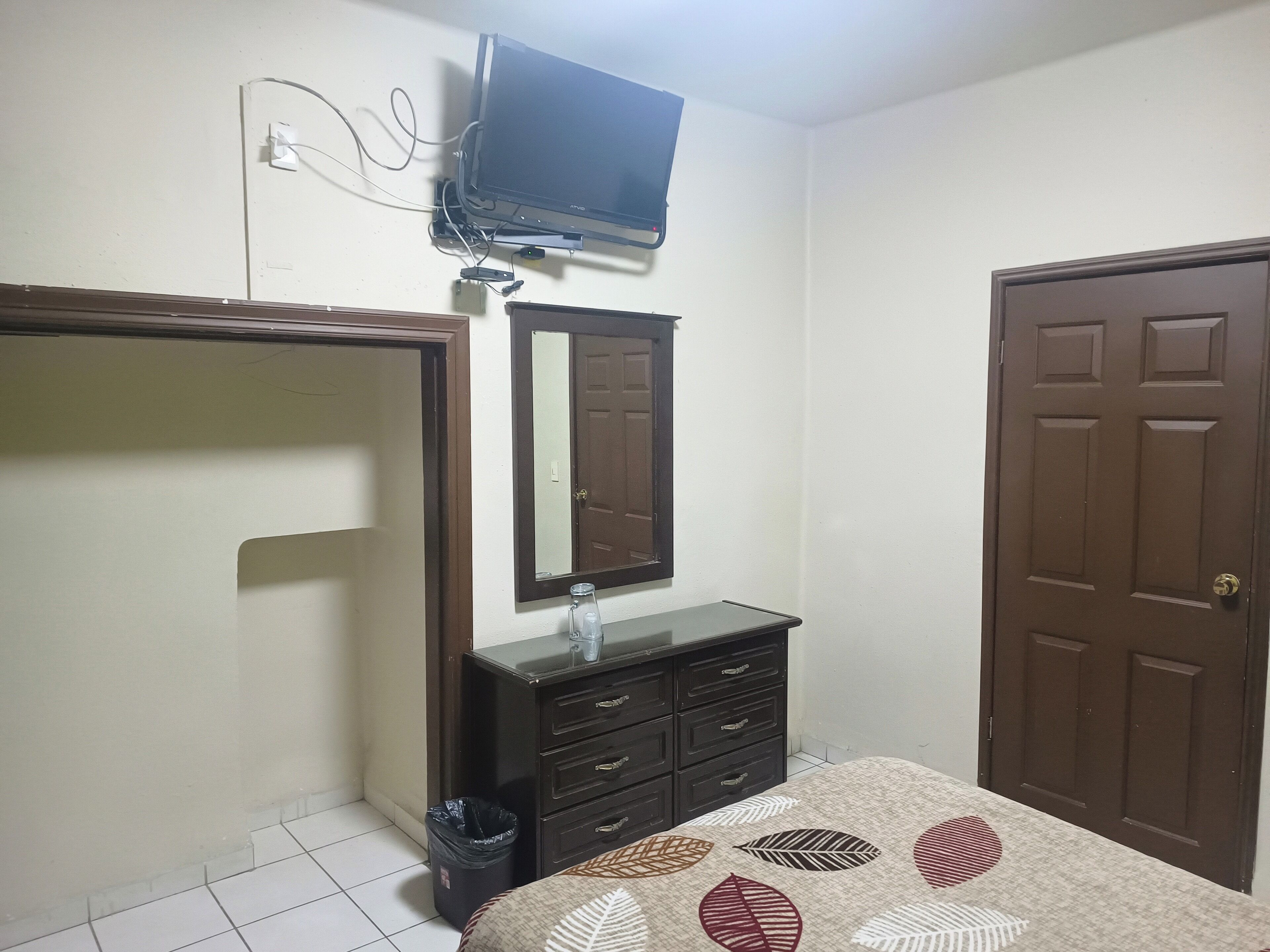A bedroom with a bed, a dresser, a mirror, a television mounted on the wall, and a door.