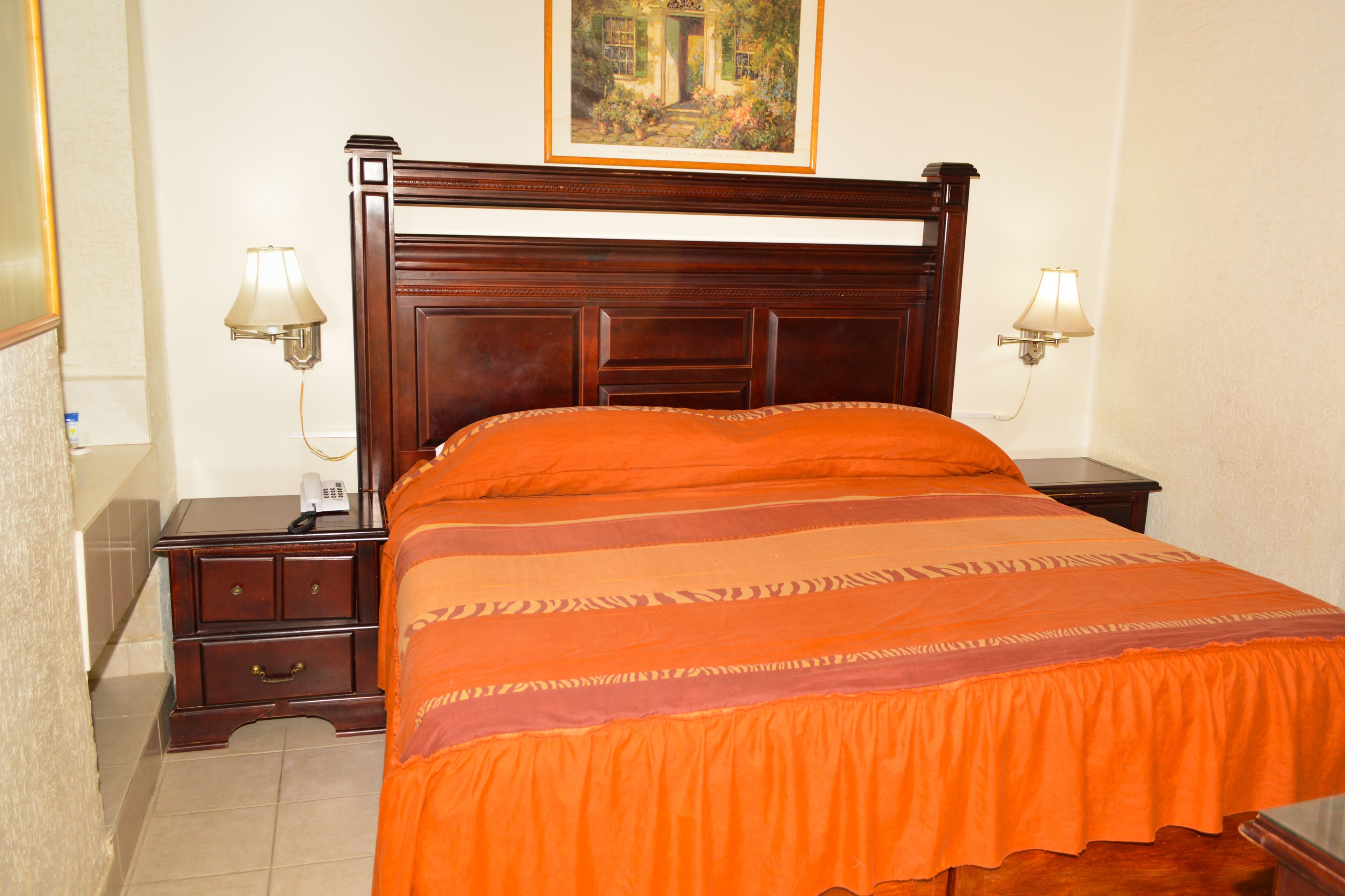 A hotel room with a wooden bed, two bedside lamps, a nightstand, and a painting on the wall.