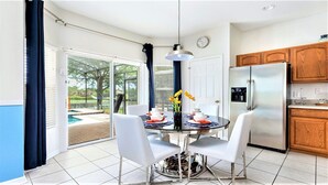 A modern kitchen with wooden cabinets, a stainless steel refrigerator, and a dining area with a glass table and white chairs.