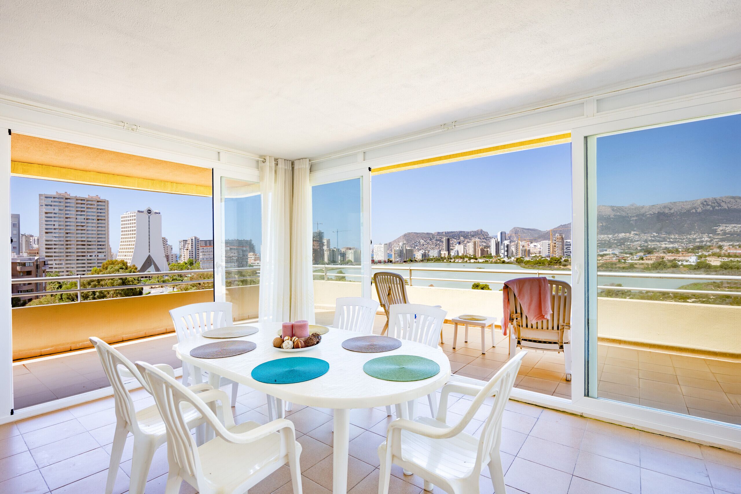 Ein geräumiger Balkon mit Blick auf die Stadt, weiße Stühle, ein runder Tisch und ein kleiner Tisch mit einem Stuhl.