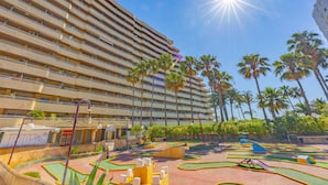 A multi-story hotel with a pool area featuring mini-golf and palm trees. - Apartment Turmalina - PlusHolidays (Calpe)