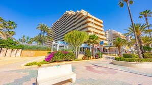 A hotel with a modern design, featuring multiple balconies and a central courtyard with palm trees and flowers. - Apartment Turmalina - PlusHolidays (Calpe)