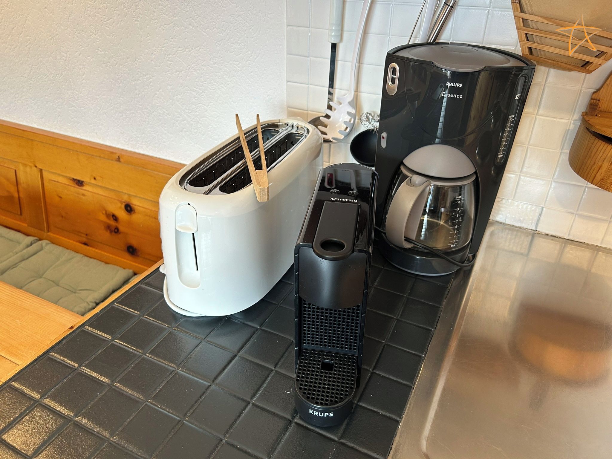 Una encimera de cocina con un tostador blanco, una cafetera negra y un molinillo de café Krups negro.
