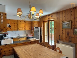 Cocina tipo cabaña de madera con una isla central, una mesa de comedor y una ventana con vistas a la vegetación.