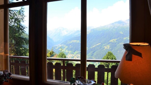 A room with a view of mountains through large windows, a wooden deck outside, and a lamp on the right. - Outside : 3-room flat for 4 persons on the 1st floor, large terrace with garden furniture.Inside : e (St-Luc)