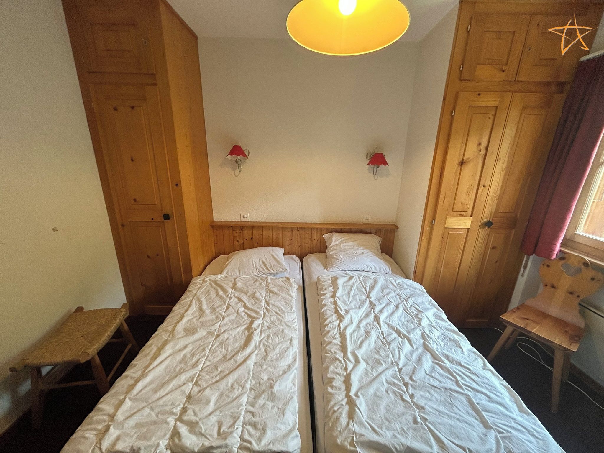A room with two beds, wooden walls, a small table, and a chair.