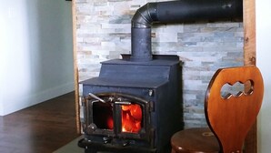 Een houtkachel met een achtergrond van een stenen muur, een houten stoel en een zwart tapijt op een houten vloer.