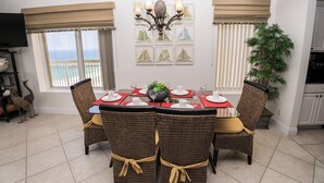 A dining area with a table set for four, surrounded by wicker chairs with yellow cushions. There is a large potted plant to the right and a wall-mounted chandelier above the table. - PARADISE ON THE OCEAN! TWO FREE BEACH CHAIR, FREE VIP PARKING SPACE! (PANAMA CITY BEACH)