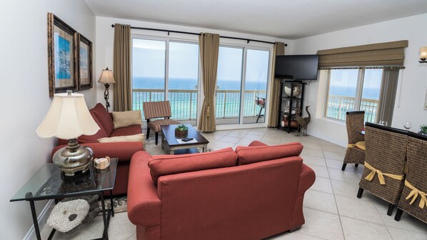 A spacious living room with a sofa, armchairs, a coffee table, and a TV. Large windows offer a view of the ocean. - PARADISE ON THE OCEAN! TWO FREE BEACH CHAIR, FREE VIP PARKING SPACE! (PANAMA CITY BEACH)