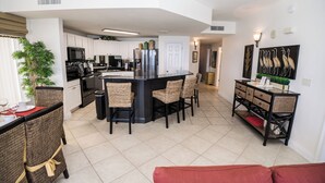 A modern kitchen with white cabinets, a black island, and wicker chairs. - PARADISE ON THE OCEAN! TWO FREE BEACH CHAIR, FREE VIP PARKING SPACE! (PANAMA CITY BEACH)