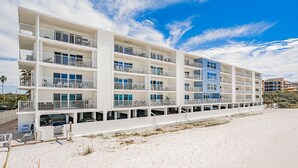 A multi-story hotel with balconies, located on a sandy beach.