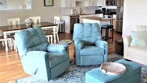 A modern living room with two blue armchairs, a dining table with chairs, and a kitchen area in the background.