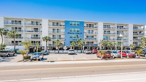 A multi-story hotel with balconies, a parking lot, and palm trees.