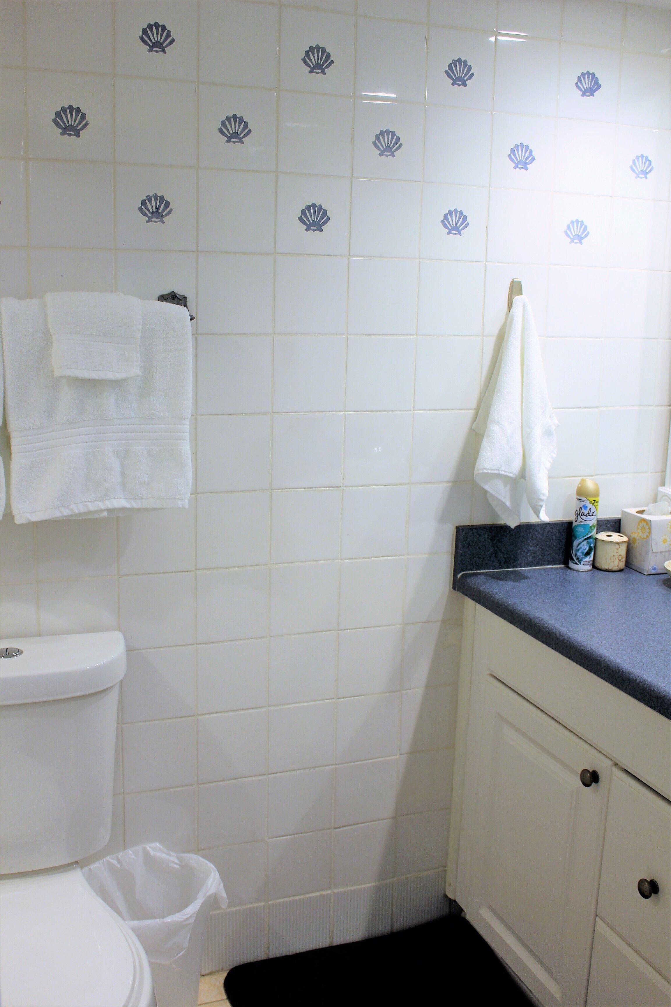 Ein Badezimmer mit weißen Fliesen, einer Toilette, einem Waschbecken mit blauer Arbeitsplatte und einem Mülleimer.