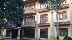 A multi-story building with a curved balcony, large windows with intricate designs, and a well-maintained lawn. - Mount House Hotel (Dikwella)