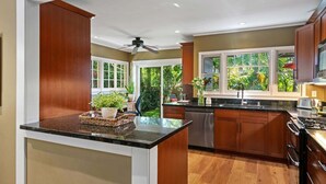 A modern kitchen with a central island, wooden cabinets, and a view of greenery outside. - Charming Home w/ Private, Enclosed Yard, Easily Accessible to All of SB! (Santa Barbara)