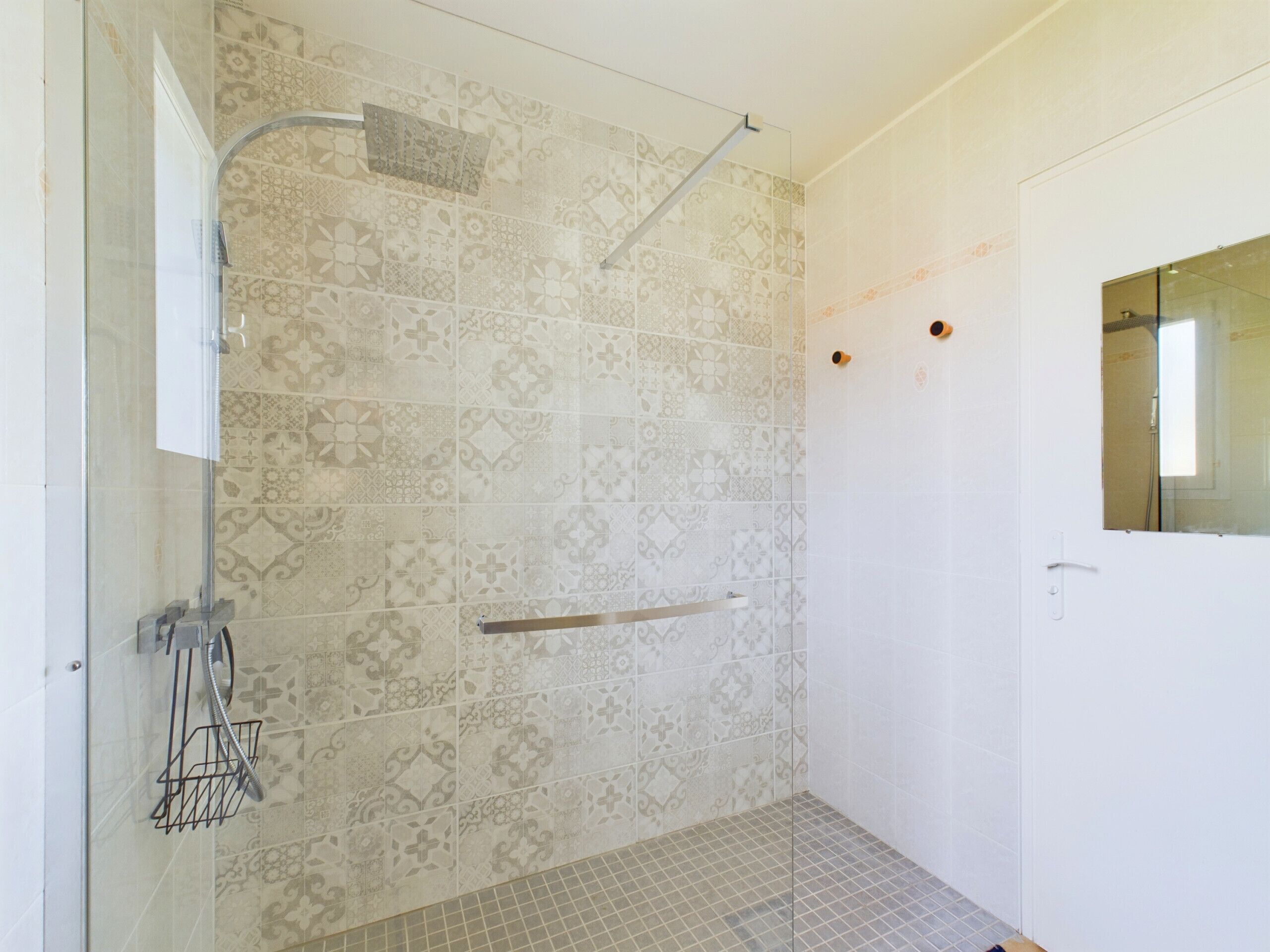 A shower with patterned tiles, a glass door, and a metal towel rack.
