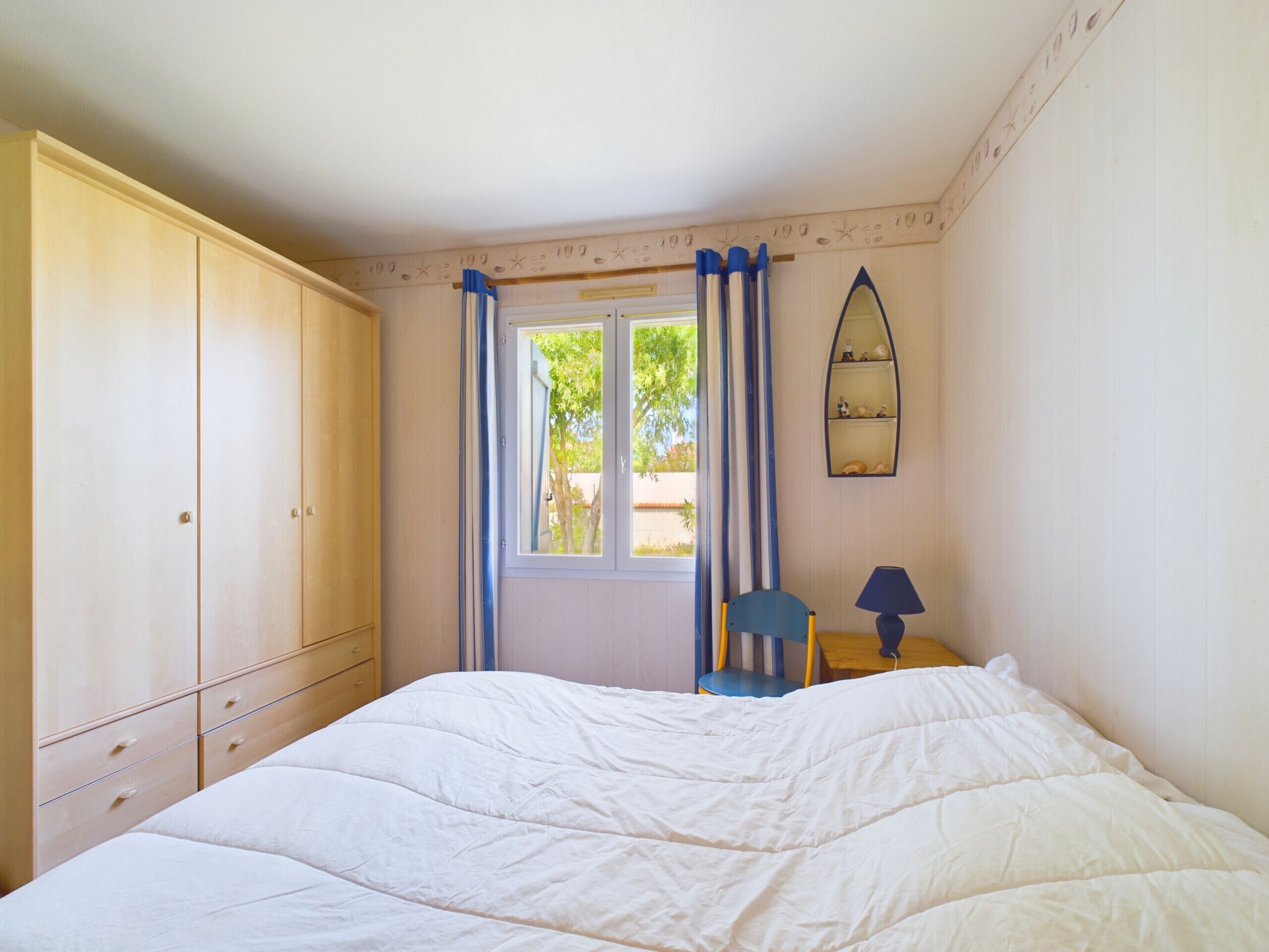 A bedroom with a bed, a wardrobe, a chair, a desk, and a window with curtains.