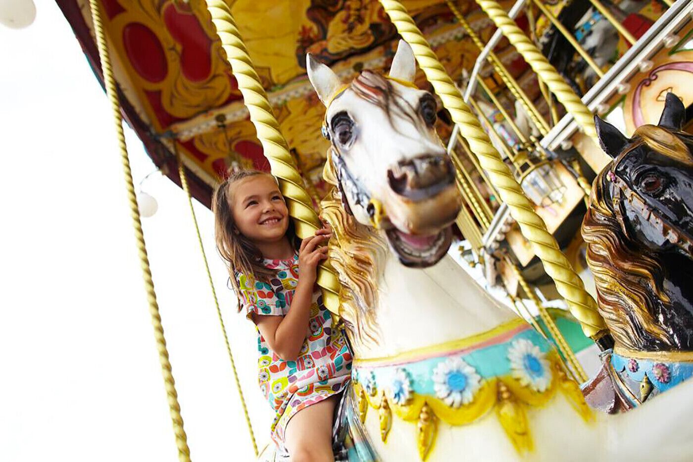Un manège avec un cheval blanc et un enfant portant une robe colorée.