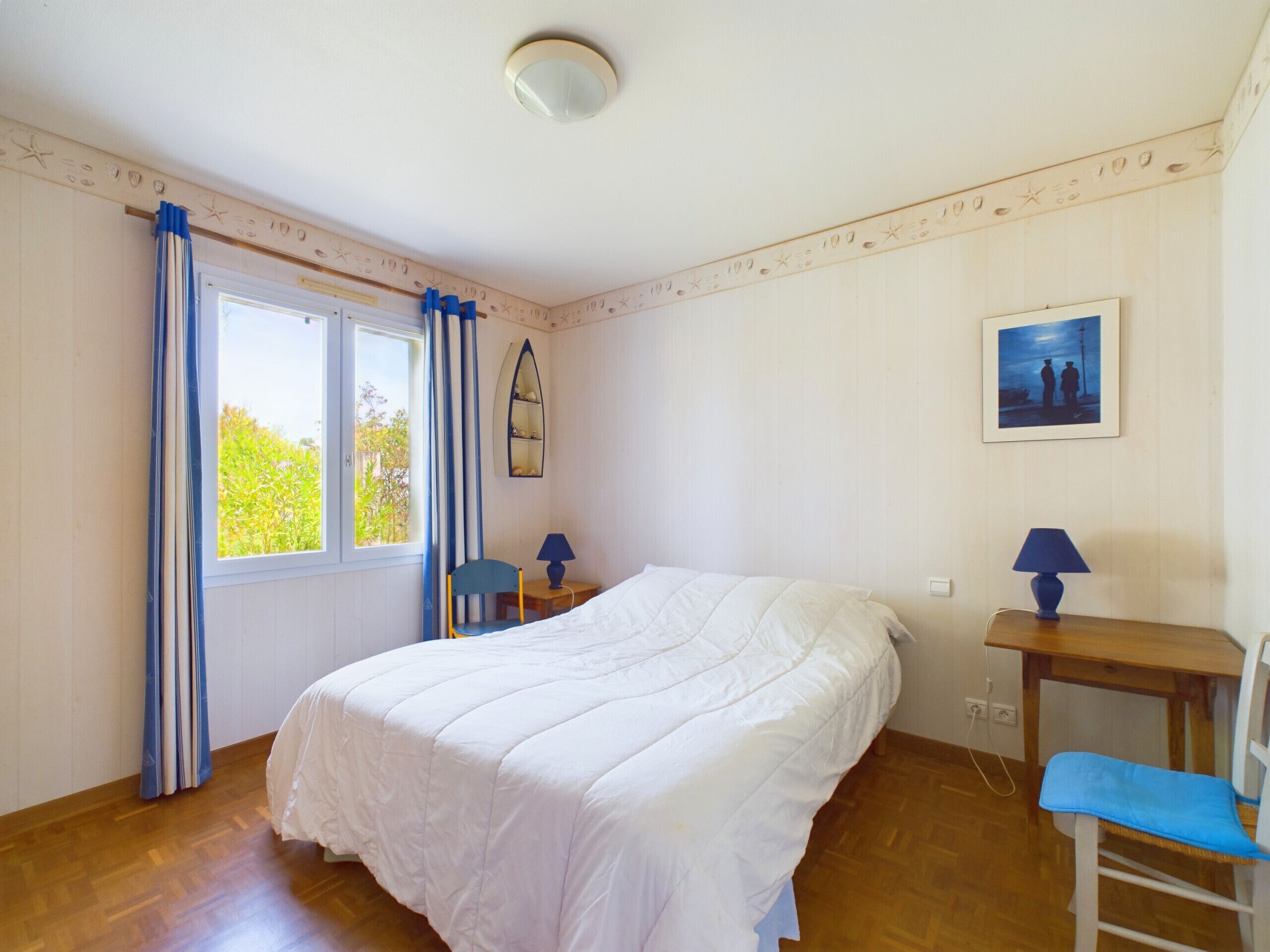 Une chambre avec un grand lit, deux tables de chevet, une chaise, une fenêtre avec des rideaux, une étagère fixée au mur et un tableau.