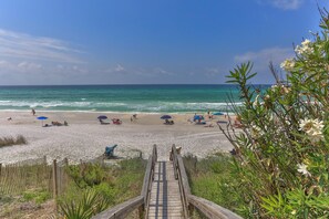 Une plage avec une promenade en bois menant au rivage, bordée de parasols et où se trouvent des gens qui se détendent.