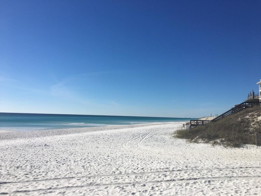 Une plage avec une promenade en bois qui mène à un bâtiment situé sur une colline de sable.