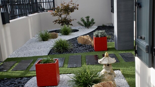 Ein moderner Garten mit Weg, verschiedenen Pflanzen und einer dekorativen Steintonne.